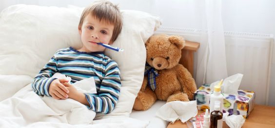 Menino deitado na cama com um termômetro na boca