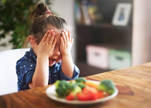 menina com a mão no rosto não querendo comer legumes