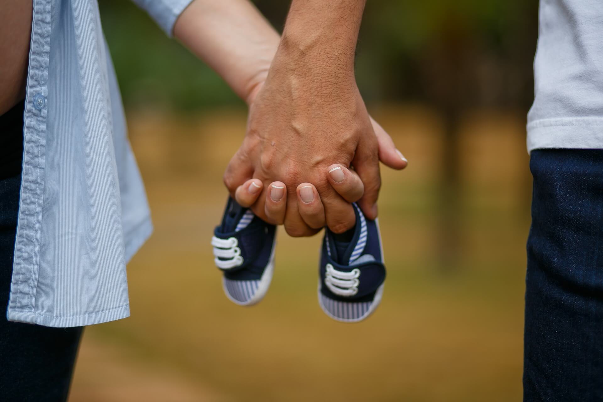 casal de mãos dadas segurando os sapatinhos do futuro bebê