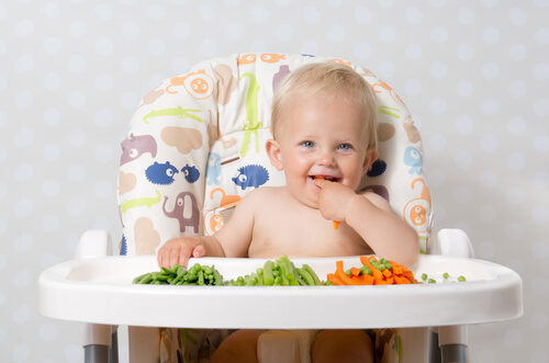 bebê sentado em uma cadeira de alimentação comendo legumes