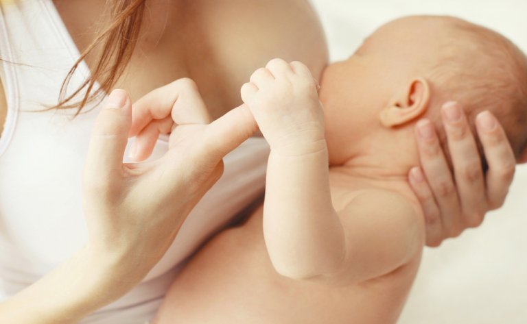 mãe segurando o dedo do bebê enquanto o amamenta