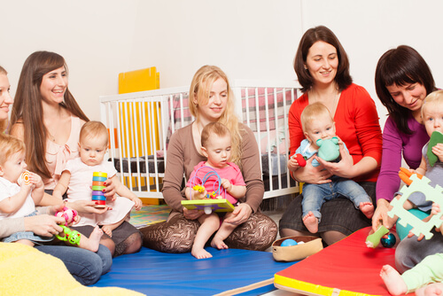 mãe sentadas no chão da creche com seus filhos no colo