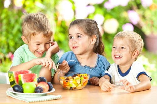 Três crianças juntas comendo um salada de frutas