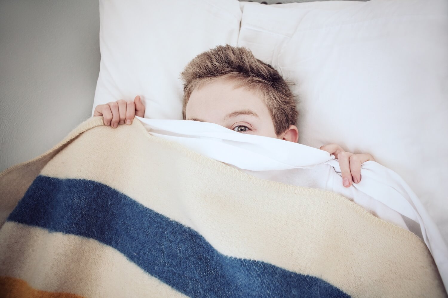 menino na cama se escondendo sob os lençóis com medo