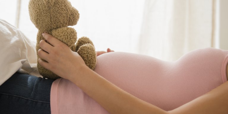 mulher grávida com ursinho de pelúcia sobre sua barriga