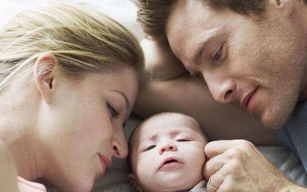 pai, mãe e bebê deitados na cama