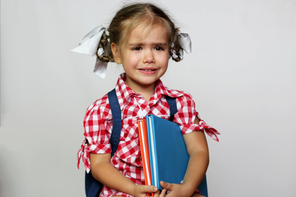 menina chorando e segurando seus livros
