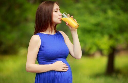 mãe grávida bebendo um copo de suco com a mão sobre a barriga