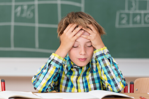 menino com dor de cabeça estudando