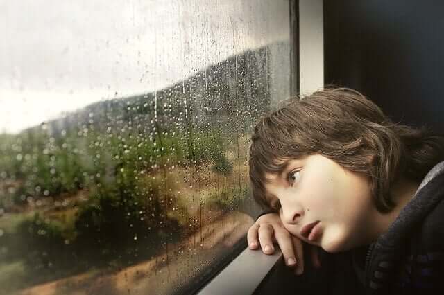 Criança cansada olhando a chuva na janela