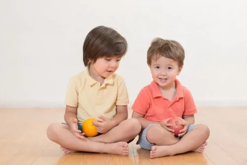 Irmãos sentados no chão com uma fruta na mão e se relacionando bem.