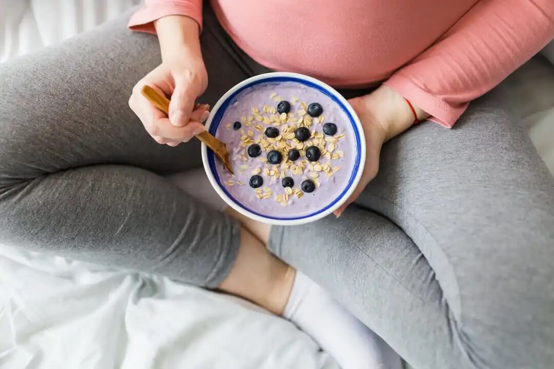 Mulher grávida comendo iogurte com cereais e frutas.