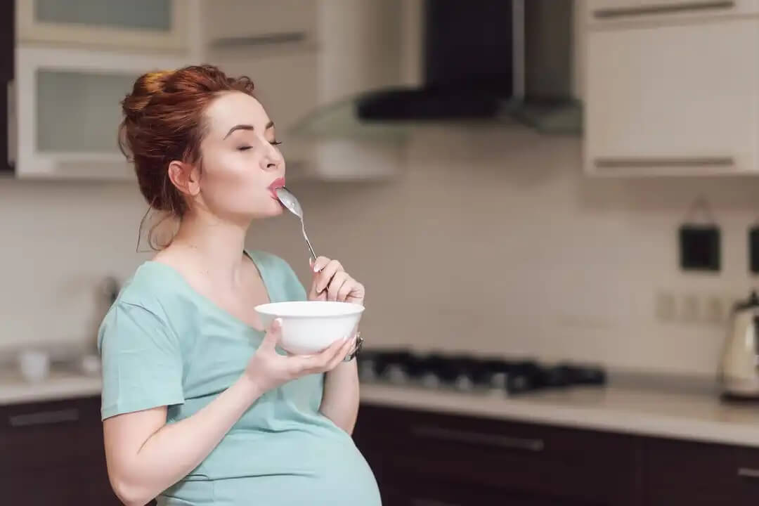 Mulher grávida desfrutando enquanto come durante o terceiro trimestre de gravidez.