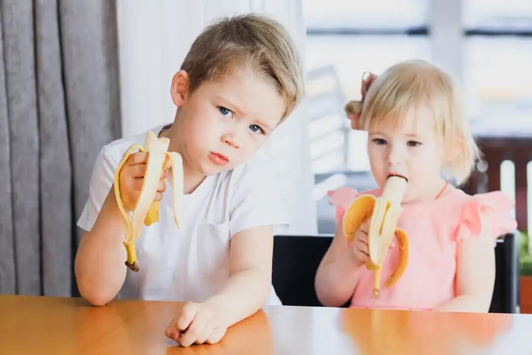 Crianças comendo uma banana cada.