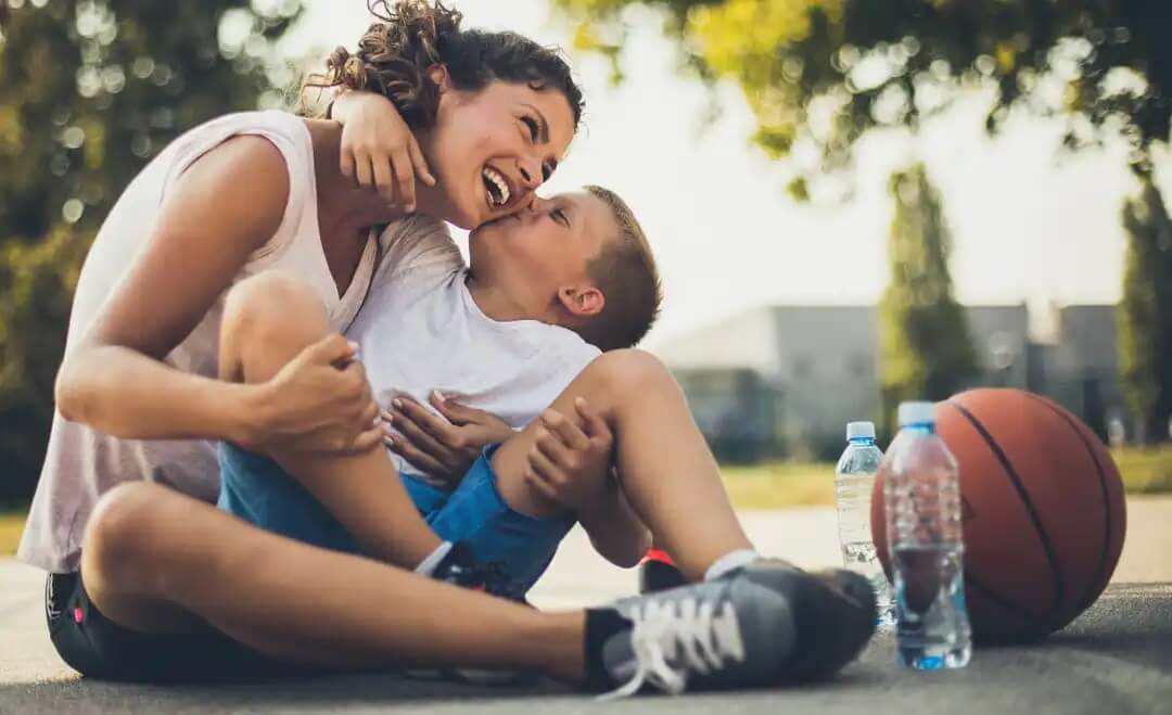 Filho dando um beijo na mãe após jogar basquete, um dos sinais de que seu filho ama você.