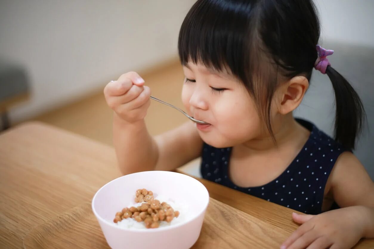 Menina comendo arroz e leguminosas.