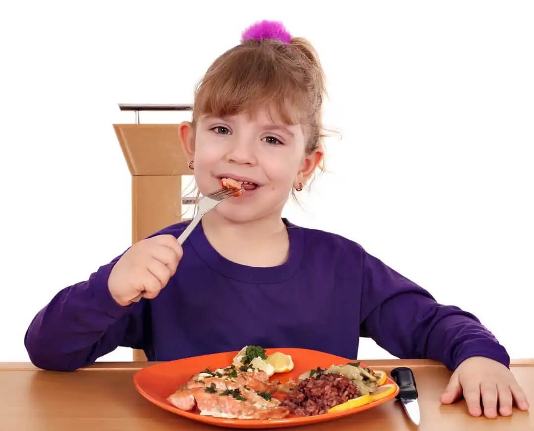 Menina comendo salmão, um dos alimentos que cuidam do coração da criança.