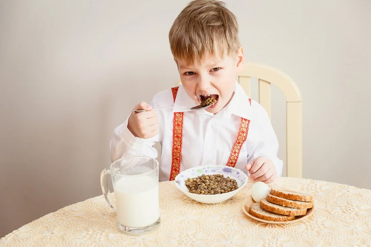 Criança comendo lentilhas porque as leguminosas são muito importantes.