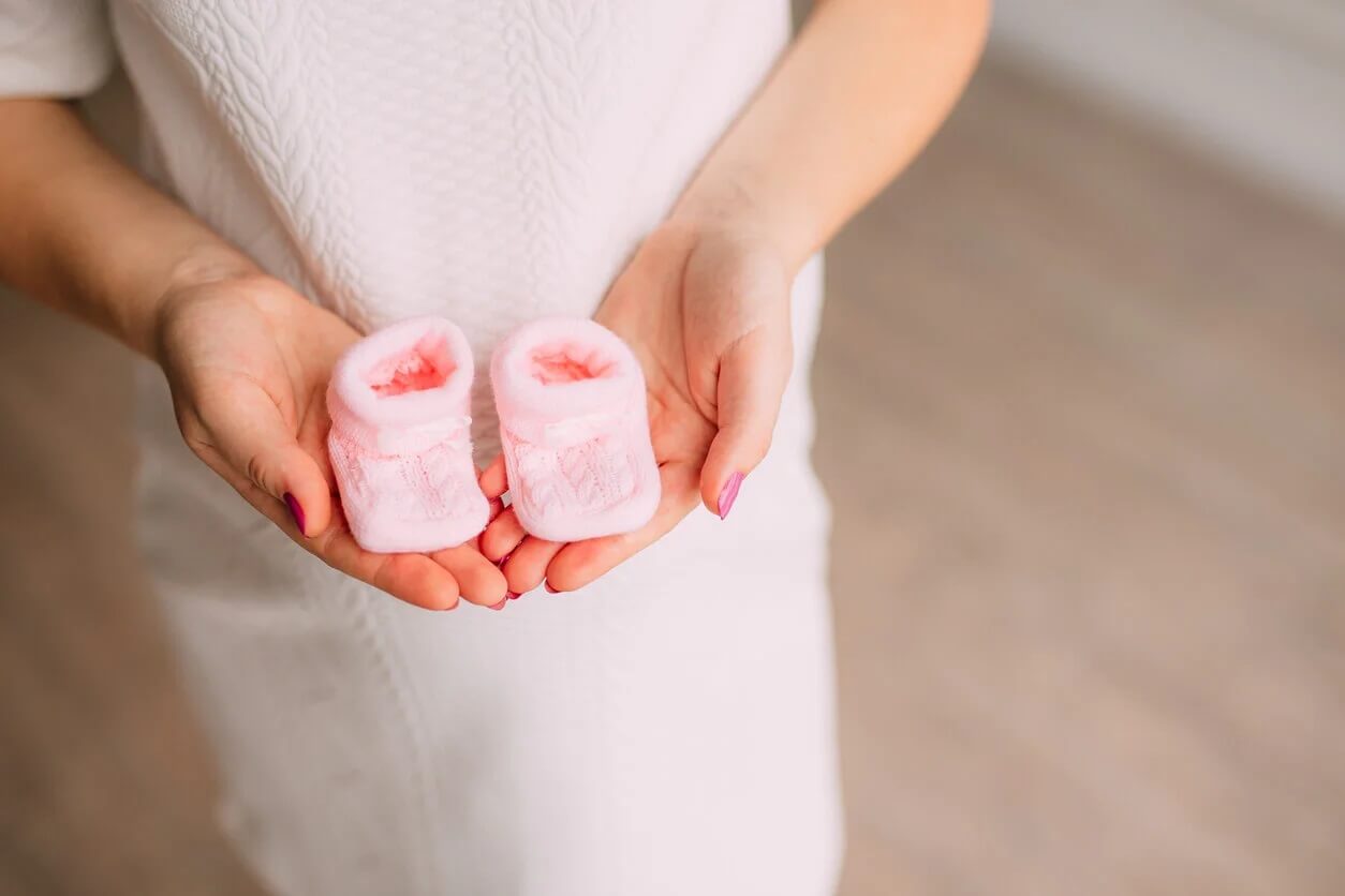 Mulher grávida com sapatinho rosa nas mãos.