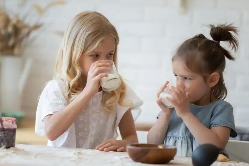 Raparigas a tomarem um copo de leite de acordo com a quantidade adequada para a idade.