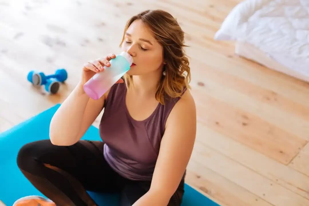 Mulher bebendo água após uma sessão de exercício após o parto.