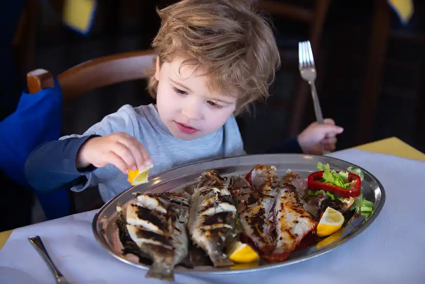 Criança comendo peixe porque é muito importante na alimentação infantil.